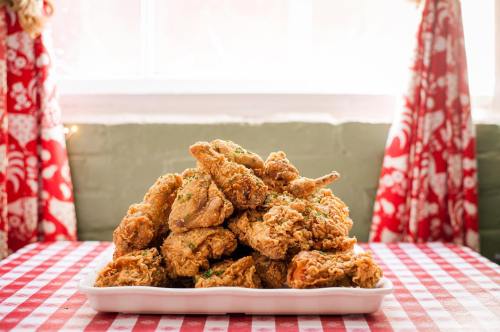 A large platter of golden fried chicken pieces garnished with herbs, set on a checkered tablecloth near a window.