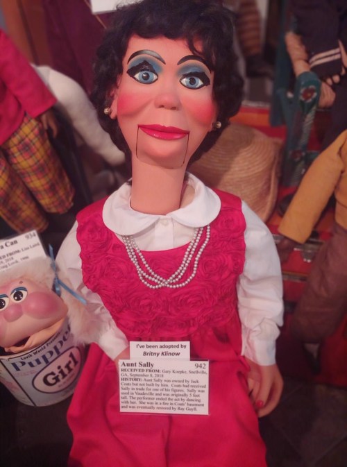 A ventriloquist puppet named Aunt Sally, wearing a pink dress and pearls, with a sign indicating adoption by Britny Klinow.
