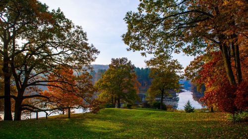 A serene landscape featuring colorful autumn trees by a calm river, with a clear sky in the background.