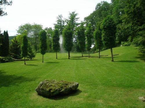 A serene landscape featuring neatly trimmed trees on a lush green lawn, with a large rock in the foreground.