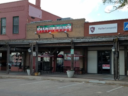 Exterior of Bella Italia Ristorante with an "Open" sign, surrounded by other storefronts and outdoor seating.