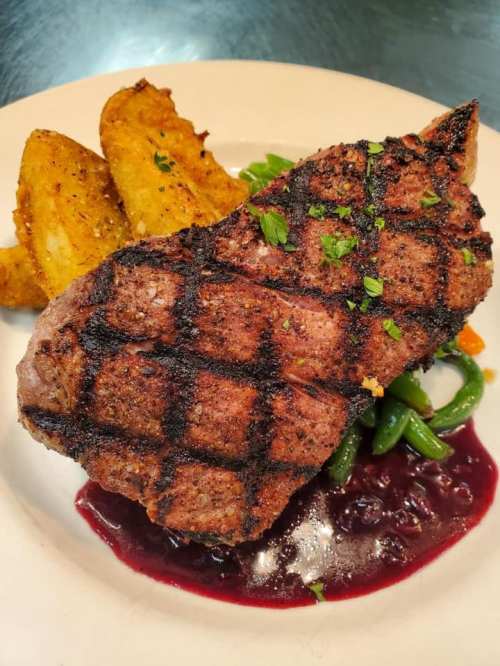 Grilled steak with a charred crust, served with green beans, colorful vegetables, and crispy potato wedges.