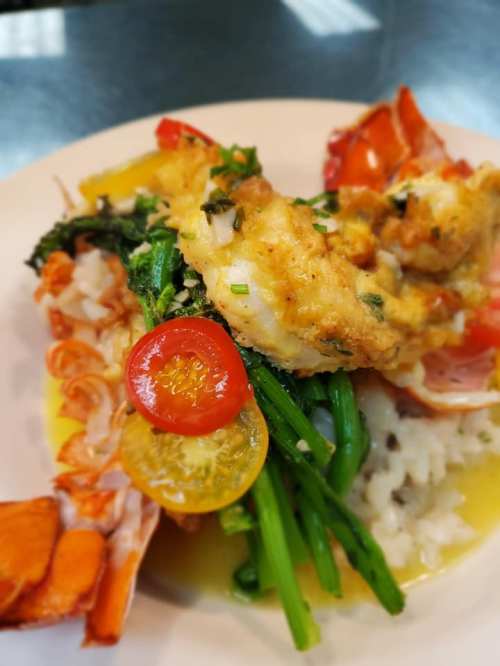 A plate of seafood featuring fried fish, lobster, cherry tomatoes, and greens served over rice in a flavorful sauce.