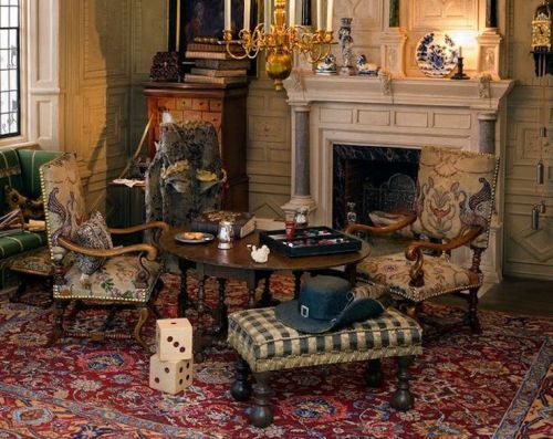 A cozy sitting room with ornate chairs, a wooden table, a fireplace, and a patterned rug, featuring dice and a hat.
