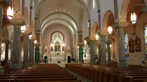 Interior of a grand church featuring tall arches, stained glass windows, and wooden pews leading to an ornate altar.