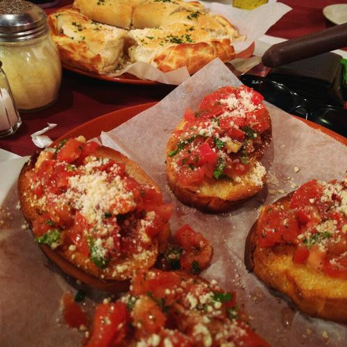 A plate of bruschetta topped with tomatoes and cheese, alongside a basket of breadsticks in the background.