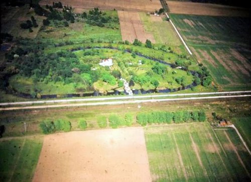 Aerial view of a lush, green landscape with a winding river, fields, and a small house surrounded by trees.