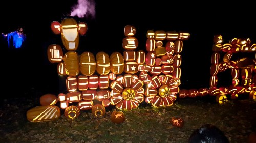 A train made of carved pumpkins, illuminated in the dark, with intricate designs and glowing orange light.