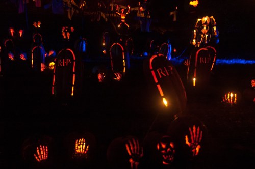 A spooky Halloween scene with glowing tombstones, carved pumpkins, and eerie decorations in a dark setting.