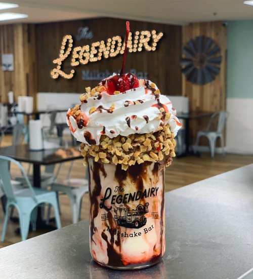 A decadent milkshake topped with whipped cream, a cherry, and crushed nuts, served in a glass at a cozy diner.
