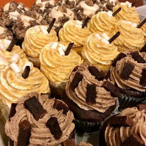 A variety of cupcakes: golden swirled frosting with marshmallows and chocolate cupcakes topped with chocolate pieces.