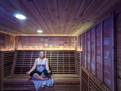 A person meditating in a wooden sauna with soft lighting and a serene atmosphere.
