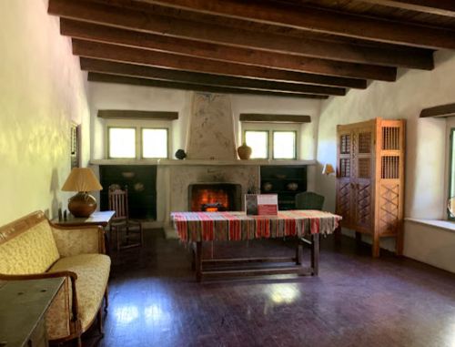 Cozy room with a fireplace, wooden beams, a table with a colorful tablecloth, and rustic furniture.