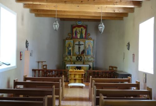 Interior of a simple chapel featuring wooden beams, pews, and an altar with religious icons.