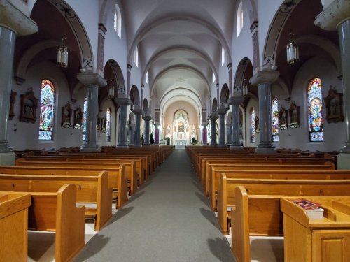 Interior of a church featuring wooden pews, arched ceilings, and stained glass windows, leading to an altar.