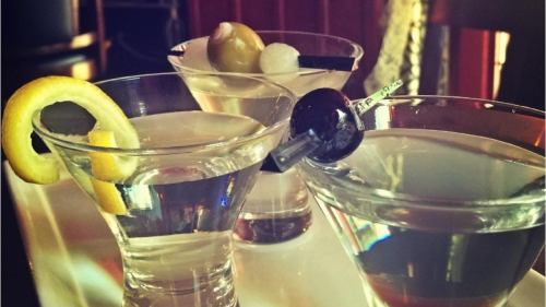 Three elegant martini glasses with garnishes of lemon, olives, and a cherry, set against a warm, inviting background.