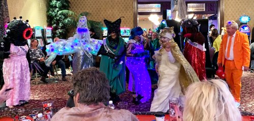 A colorful group of costumed performers in a casino, featuring lights and unique outfits, entertaining an audience.