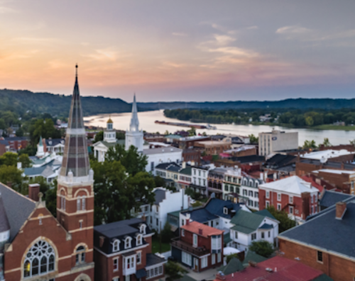 Aerial view of a riverside town at sunset, featuring historic buildings and church steeples along the water.