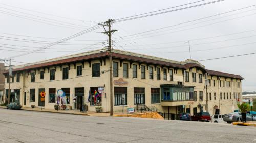 Historic building on a sloped street, featuring multiple storefronts and power lines overhead.