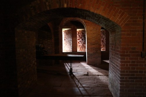 Dimly lit brick room with arched doorways and a table, creating a mysterious atmosphere.