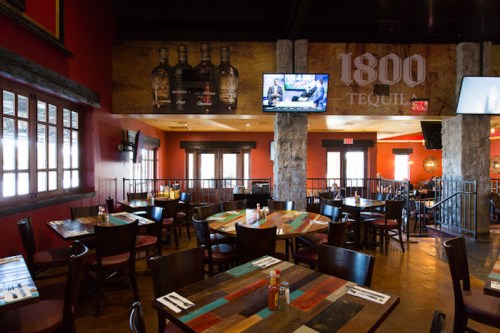 Interior of a restaurant featuring wooden tables, stone accents, and a bar area with tequila bottles displayed.