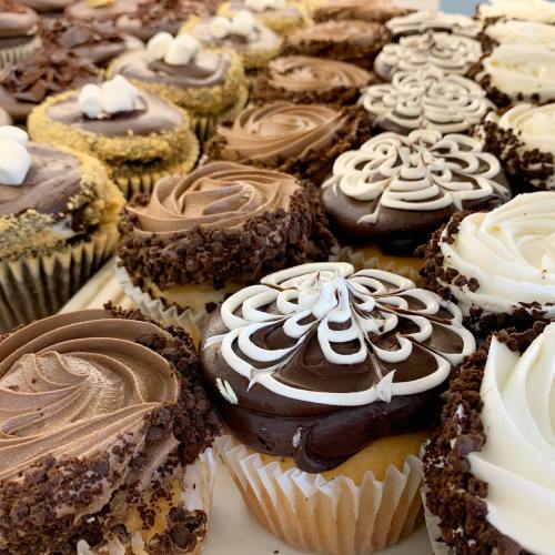 A variety of decorated cupcakes with chocolate and vanilla frosting, featuring swirls and toppings, displayed on a tray.