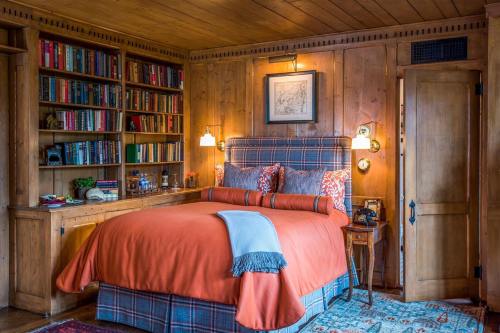 Cozy bedroom with wooden walls, a plaid bedspread, bookshelves, and warm lighting, creating a rustic atmosphere.