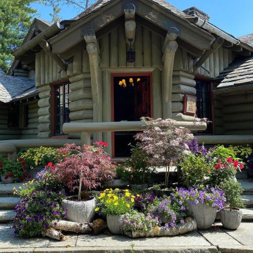 A charming log cabin with a flower-filled garden at the entrance, featuring colorful blooms and rustic architecture.