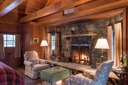 Cozy cabin interior with a stone fireplace, two patterned chairs, and warm wooden accents, creating a welcoming atmosphere.