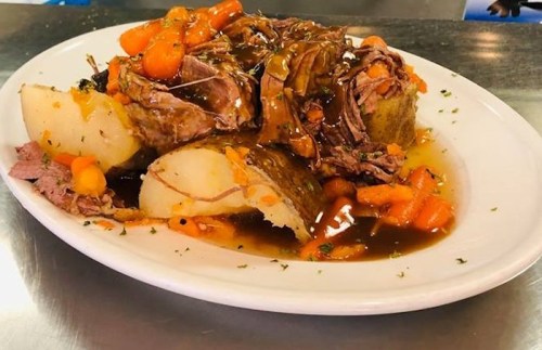 A plate of tender beef roast with carrots and gravy served over mashed potatoes, garnished with herbs.