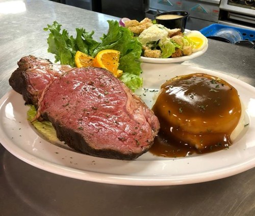 A plate featuring a juicy prime rib, gravy, a side of mashed potatoes, fresh salad, and orange slices.