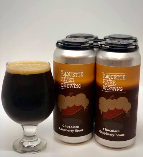 A glass of dark stout next to a four-pack of Raquette River Brewing's Chocolate Raspberry Stout cans.