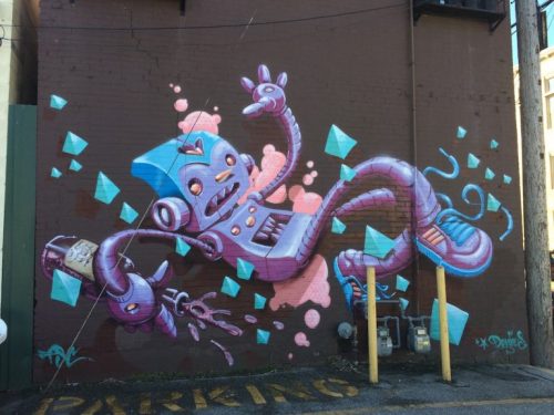 Colorful mural of a playful robot surrounded by geometric shapes, spray painting on a brick wall.