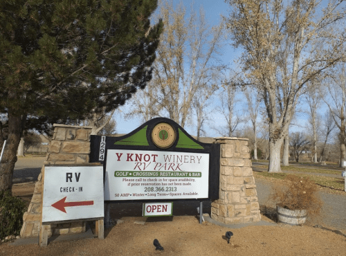 Sign for Y Knot Winery RV Park with directions for check-in and information about amenities. Trees in the background.