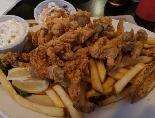 A plate of fried food featuring crispy fried oysters, French fries, coleslaw, and dipping sauces.