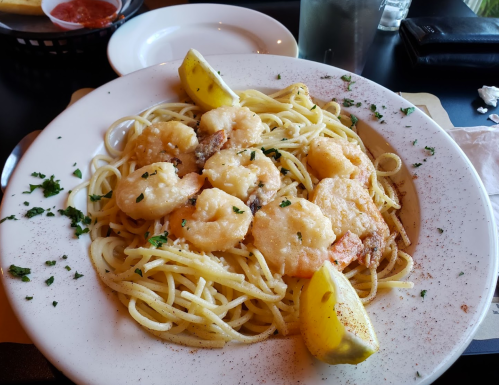 A plate of shrimp pasta with lemon wedges, garnished with parsley, served in a restaurant setting.