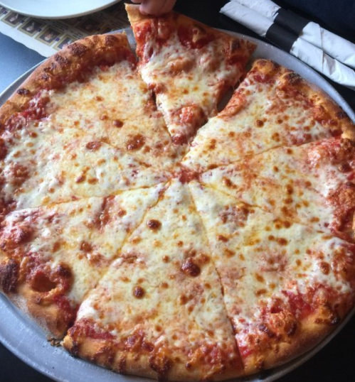 A large cheese pizza with a slice being lifted, served on a round metal tray.