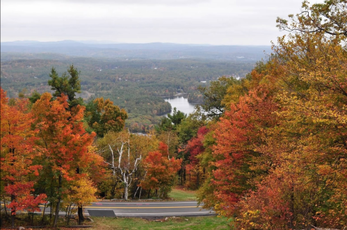 Scenic view of a colorful autumn landscape with trees in vibrant fall colors and a winding road overlooking a lake.