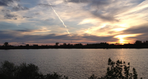 A serene sunset over a calm lake, with colorful clouds and silhouettes of trees along the shore.