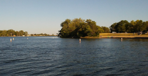 A calm river scene with trees along the shore and a sandy beach under a clear blue sky.