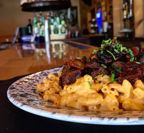 A plate of creamy macaroni and cheese topped with savory beef, garnished with chopped chives, in a bar setting.