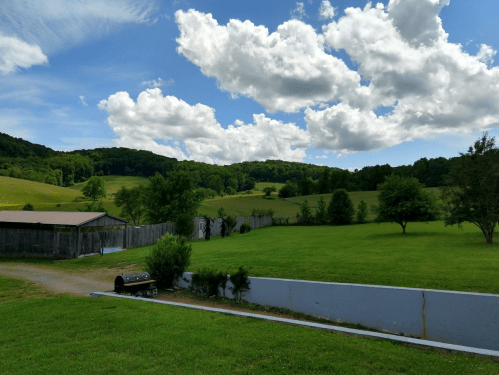 A scenic landscape featuring green fields, trees, and a blue sky with fluffy clouds. A barn is visible in the background.