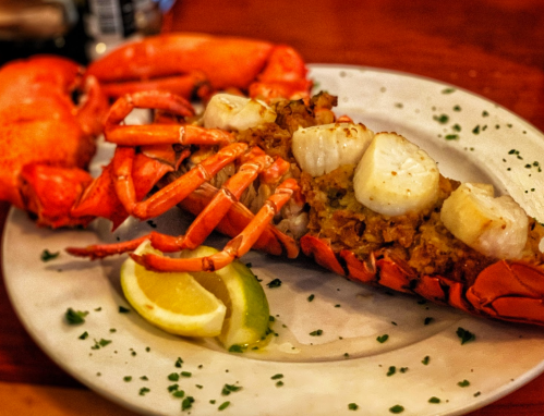 A plate featuring a lobster tail stuffed with scallops, garnished with lemon wedges and parsley.