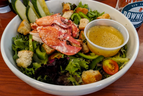 A fresh salad with lobster, greens, croutons, bell peppers, and a side of dressing in a bowl.