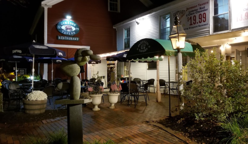 Exterior view of Jameson Tavern at night, featuring outdoor seating, decorative lights, and a stone sculpture.