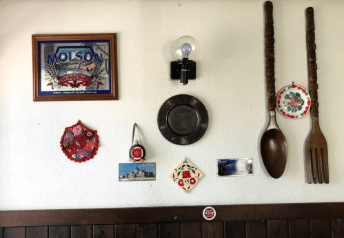 A wall display featuring a Molson sign, decorative plates, postcards, and large wooden utensils.