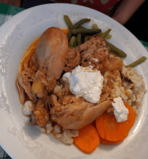 A plate of chicken with gravy, carrots, green beans, and a dollop of sour cream over a bed of rice or grains.
