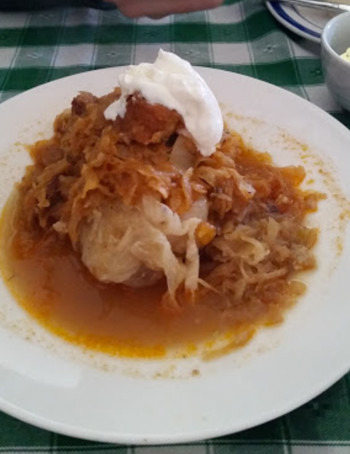 A plate of dumplings topped with sauerkraut and a dollop of sour cream, served in a savory sauce.
