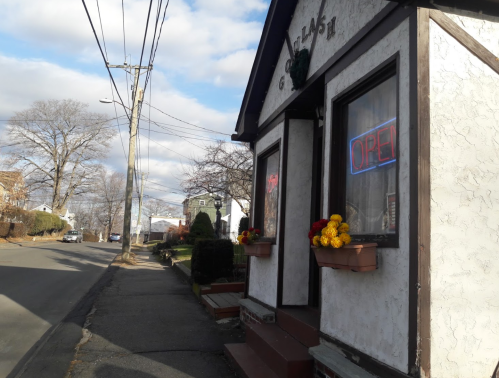 A small building with an "OPEN" sign, flower pots, and power lines, set along a quiet street on a cloudy day.