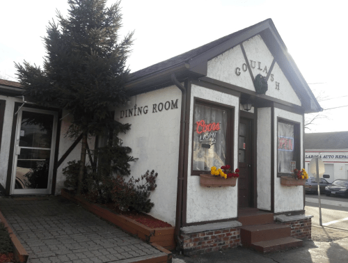 Exterior of a restaurant named "Goulash," featuring a sign, flowers, and a tree in front.